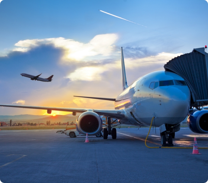 Aeroplane at gate at sunset with plane taking off in the background