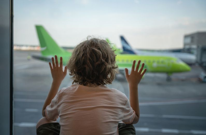 Child looking out at green aircraft from airport terminal